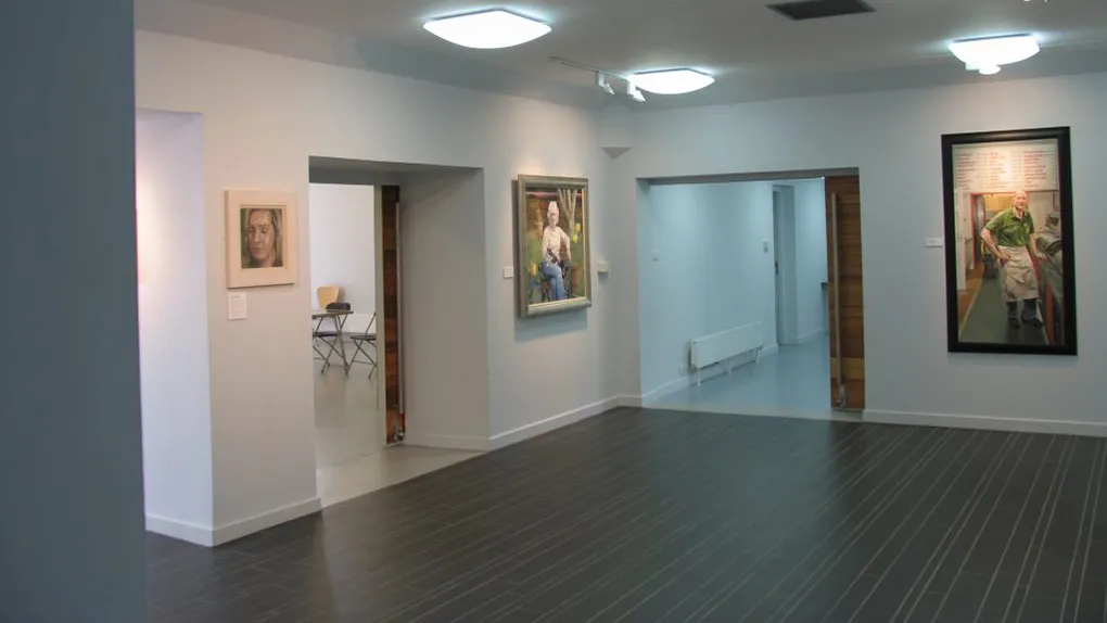 A gallery space with white walls, two doorways and paintings on the walls